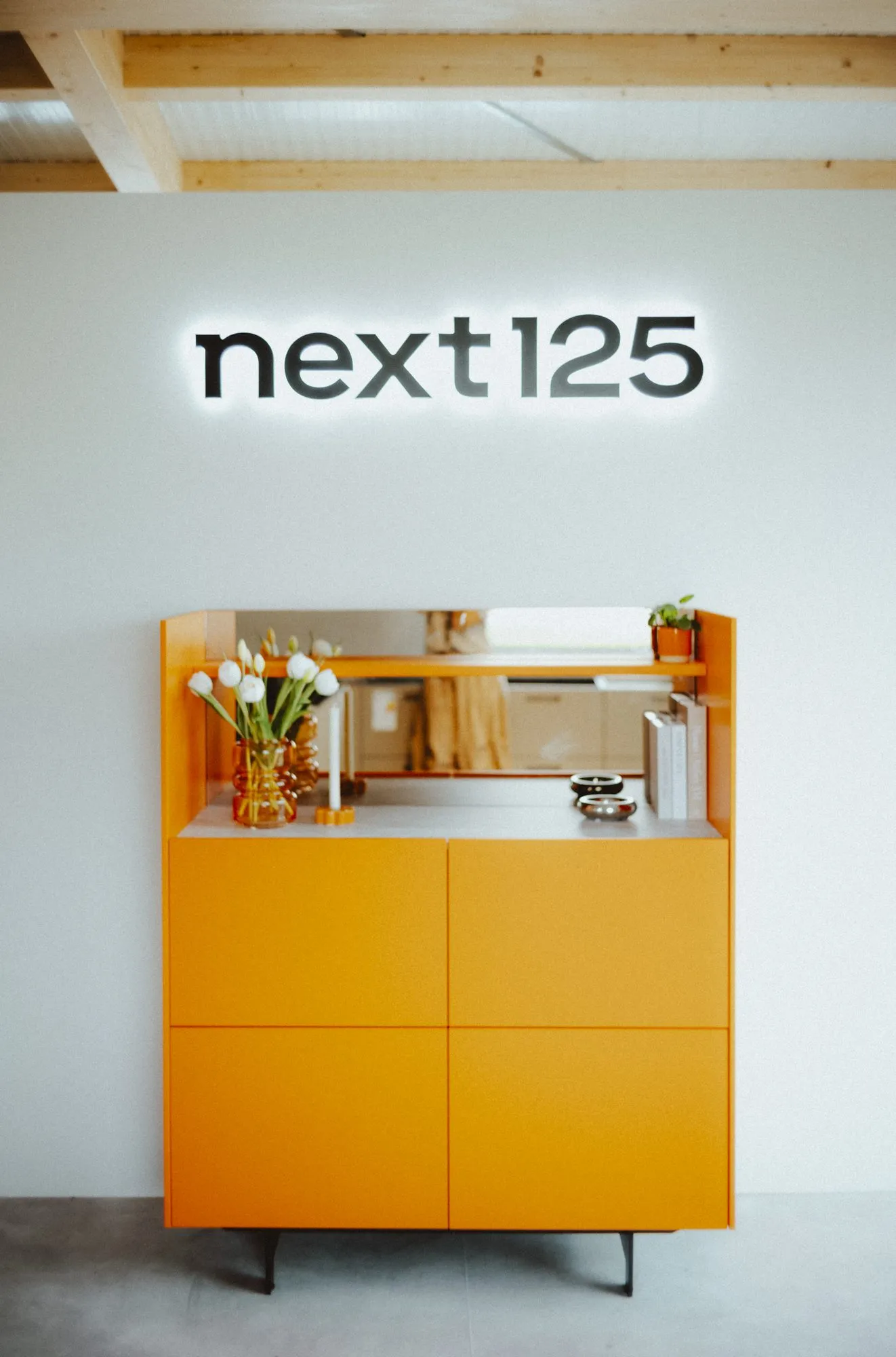 Schriftzug next125 über einem orangefarbenen Sideboard