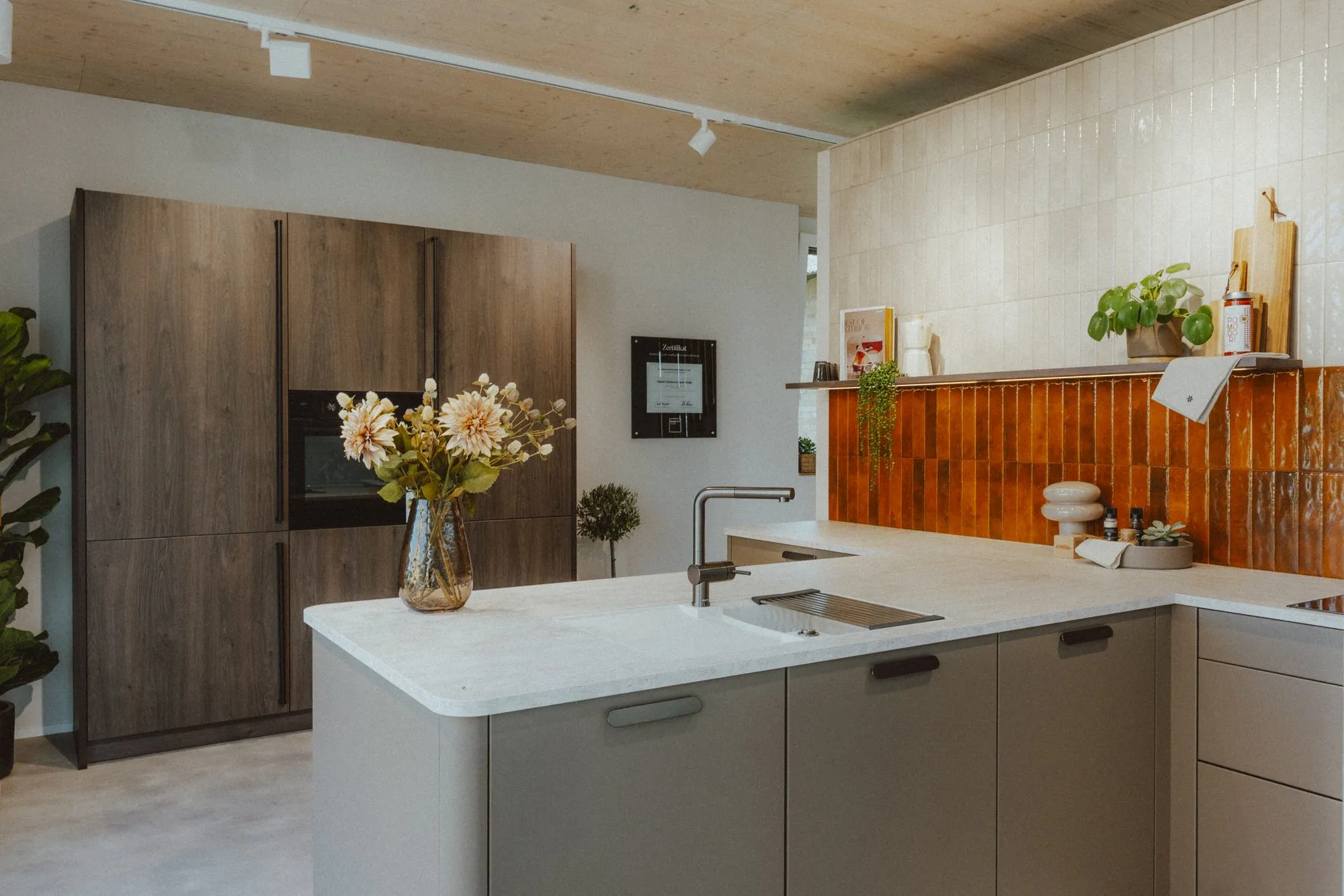 Küche mit Fliesenrückwand, heller Arbeitsplatte und Hochschränken in dunklem Holz